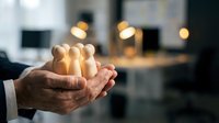 Businessman hands protecting wooden human figures in modern office environment symbolizing team leadership, employee care and human resources management.