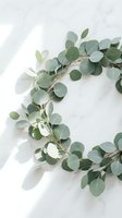 Fresh eucalyptus wreath with round silver dollar leaves arranged in a circle on a white marble surface with soft natural light.