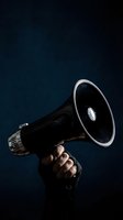 Hand holding black megaphone against dark blue background for communication and announcement concepts in business marketing campaigns.