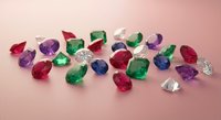 Collection of colorful precious gemstones including emeralds, rubies, sapphires and diamonds scattered on pink surface for jewelry making and luxury design.