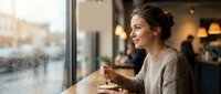 Young woman enjoying coffee in cozy cafe by window on rainy day, warm atmosphere perfect for relaxation and contemplation in modern coffee shop interior.