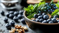 Fresh blueberries and blackberries in ceramic bowl with mint leaves and scattered nuts on dark background, healthy breakfast ingredients for smoothie bowl.