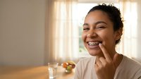 Young African American woman with dental braces smiling while applying skincare cream in bright modern bathroom during morning routine.
