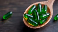 Green translucent soft gel capsules on wooden spoon against dark background, macro view of dietary supplements and vitamins for health and wellness.