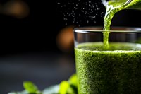 Fresh green smoothie being poured into glass with vibrant healthy drink for detox nutrition and wellness lifestyle on dark background.