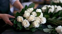 Fresh white roses bouquet with green leaves being arranged by florist hands, romantic floral composition for wedding or special occasion celebration.