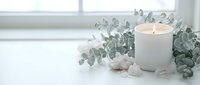 Burning white candle with eucalyptus branches and crystals on clean surface creating peaceful spa atmosphere for relaxation and wellness rituals.