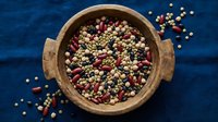 Mixed legumes and beans in rustic wooden bowl on blue textile background. Colorful assortment of lentils, chickpeas and kidney beans for healthy cooking and nutrition.