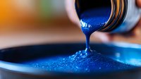 Vibrant blue paint or ink pouring from container creating smooth glossy stream with dynamic surface texture and ripples against dark background.