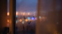Raindrops on window glass with blurred city lights creating bokeh effect during evening twilight for cozy indoor atmosphere and weather concepts.