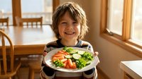 Young boy with blonde hair smiling while holding plate of fresh vegetables in bright kitchen. Healthy eating concept for children nutrition education.