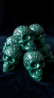 Group of ornate emerald green skulls with intricate floral filigree patterns arranged on dark textured surface. Decorative metallic skull sculptures for gothic, Halloween, or alternative design projects.