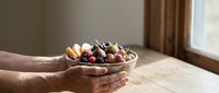 Hands holding glass bowl filled with assorted chocolate truffles and candies on wooden table near window for gourmet dessert presentation.