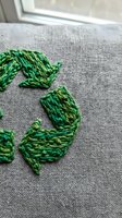 Green embroidery thread forming decorative leaf pattern on natural linen fabric near window, handmade needlework craft project for home decor and textile art.