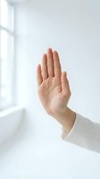 Hand raised in stop gesture against white wall with natural window light for communication and body language concepts.