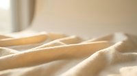 Soft beige fabric with gentle folds and warm sunlight creating shadows and highlights on textile surface for interior design and home decor projects.