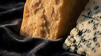 Aged artisan cheese varieties with blue veins and crystalline texture on dark fabric background for gourmet food photography and culinary presentations.