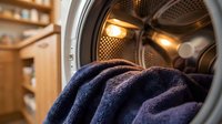 Purple towels inside open washing machine drum with warm lighting creating cozy laundry room atmosphere for household cleaning and domestic care concepts.