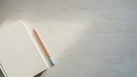 Blank notebook with lined pages and wooden pencil on white wooden desk surface, overhead flat lay composition for writing, planning, education, and creative projects.