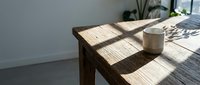 Wooden table with ceramic mug in sunlit room, casting natural shadows across surface for interior design and lifestyle content.