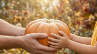 Hands of adult and child holding orange pumpkin together in autumn field, celebrating harvest season and family bonding outdoors.