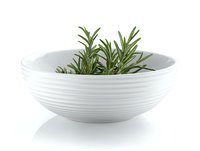 Fresh rosemary sprigs in modern white ceramic bowl with ribbed texture pattern on white background, isolated culinary herb for cooking and aromatherapy.