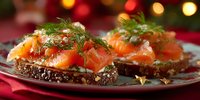 Delicious salmon sandwiches with cream cheese and fresh dill on dark bread, served on festive plate with holiday lights in background.