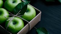 Fresh green apples with leaves in kraft paper box tied with rustic twine string on dark wooden background. Natural organic produce styling for food photography.