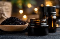Black caviar in wooden bowl with essential oil bottles on dark background, illuminated by warm bokeh lights. Luxury gourmet food styling and spa concept.