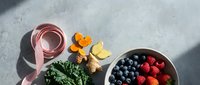 Healthy lifestyle flat lay with fresh berries, leafy greens, turmeric root, lemon and measuring tape on concrete surface for wellness nutrition concept.