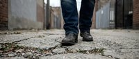 Person walking on cracked urban pavement with worn boots in city alley. Concept of journey, determination, and overcoming challenges in urban environment.