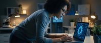 Young African American woman software developer coding on laptop with glowing blue code display in modern home office workspace during evening hours.
