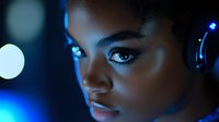 Young African American woman with headphones in dramatic blue lighting, close-up portrait showing intense gaze and glowing skin texture against dark background.