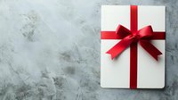 Elegant white gift box with vibrant red ribbon and bow on textured gray concrete background for holiday, birthday, or special occasion celebration.