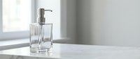 Clear glass soap dispenser with chrome pump on white marble countertop in modern bathroom with natural window light for home decor and hygiene products.
