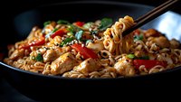 Chopsticks lifting steaming Asian noodles with chicken, colorful bell peppers, and sesame seeds in dark bowl against black background, moody food photography.