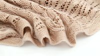 Delicate beige knitted lace fabric with intricate openwork pattern showing detailed texture and soft folds on white background, suitable for fashion and textile design.