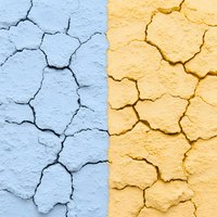 Cracked wall surface split in blue and yellow colors showing weathered texture and deep fissures in concrete or plaster background.