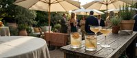 Outdoor restaurant terrace with cocktails on wooden table, umbrellas and diners in background creating warm hospitality atmosphere for dining venues.
