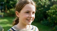 Young girl with freckles and braided hair smiling outdoors in natural park setting. Cheerful child portrait for family and lifestyle concepts.