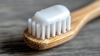 Bamboo toothbrush with white toothpaste on bristles in macro close up view against wooden surface, showing eco-friendly dental care and sustainable lifestyle.