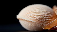 Macro shot of creamy peach ice cream scoop with delicate rippled texture against dark background, showing smooth frozen dessert details and soft curves.
