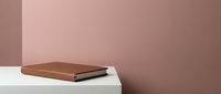 Modern minimalist product display with brown leather notebook on white surface against dusty rose pink wall background for branding and marketing presentations.