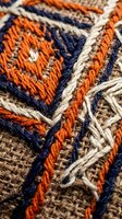 Colorful embroidered textile with orange and navy blue geometric patterns on natural burlap fabric showing detailed stitching and traditional craftsmanship techniques.