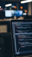 Software developer coding on laptop screen with programming code in modern office environment with blurred background lights and workspace atmosphere.