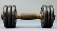 Old rusty metal dumbbell with wooden handle showing wear and patina, vintage sports equipment photographed on neutral background for fitness and strength training concept.