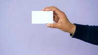 Male hand holding blank white business card against purple background for corporate branding and marketing presentations.