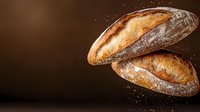 Artisan sourdough bread loaves with golden crust and flour dusting on dark background for bakery marketing and culinary photography projects.