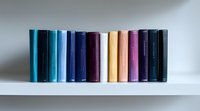 Row of colorful hardcover books standing in line on white shelf against neutral wall background, creating minimalist gradient arrangement from blue to purple tones.