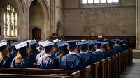Graduation ceremony in historic church with students in blue caps and gowns seated in wooden pews, celebrating academic achievement in sacred setting.